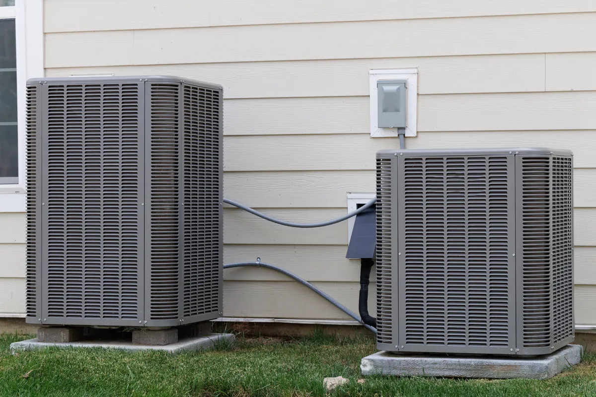 Two residential air conditioning condenser units beside a house